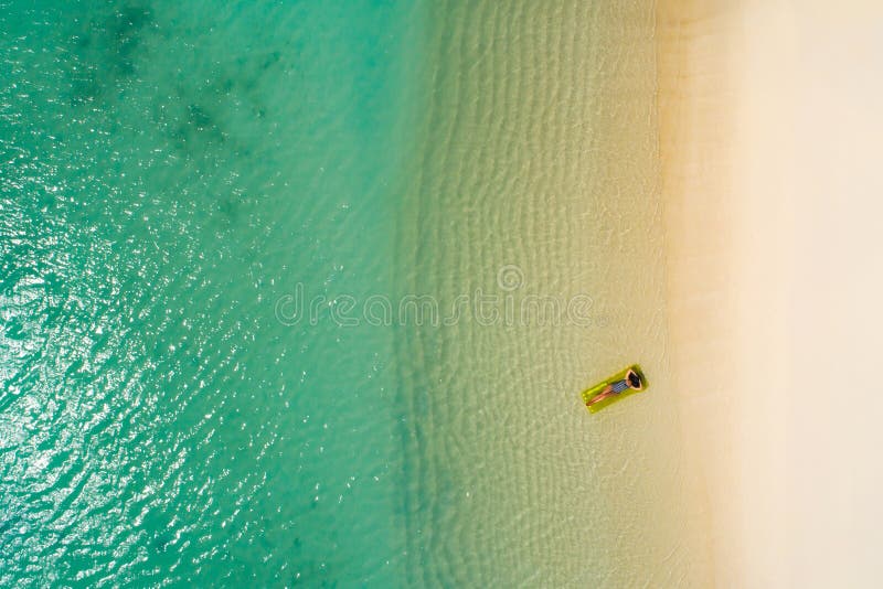 Aerial view of slim woman swimming on the swim mattress in the transparent turquoise sea in Seychelles. Summer seascape with girl, beautiful waves, colorful water. Top view from drone. Aerial view of slim woman swimming on the swim mattress in the transparent turquoise sea in Seychelles. Summer seascape with girl, beautiful waves, colorful water. Top view from drone