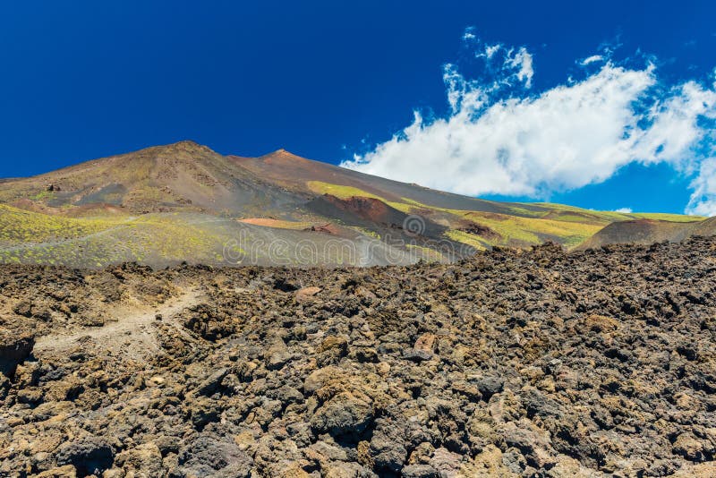 Vista scenica dell'Etna con cielo blu sui precedenti Colline e giacimento di fioritura della lava con le pietre vulcaniche La Sic fotografia stock Vista scenica dell'Etna con cielo blu sui precedenti Colline e giacimento di fioritura della lava con le pietre vulcaniche La Sic fotografia stock