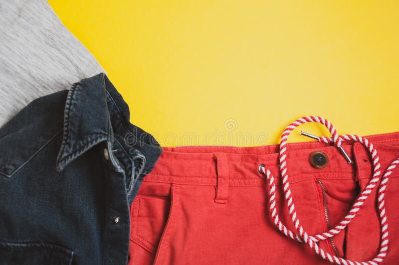 Vista superior de la camiseta gris, de la chaqueta del dril de algodón y de pantalones cortos rojos en fondo amarillo foto de archivo libre de regalías Vista superior de la camiseta gris, de la chaqueta del dril de algodón y de pantalones cortos rojos en fondo amarillo foto de archivo libre de regalías