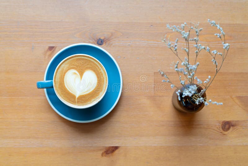 Vista superior de la taza y de la flor calientes de café con una espuma de la forma del corazón del arte del barista en fondo d imágenes de archivo libres de regalías Vista superior de la taza y de la flor calientes de café con una espuma de la forma del corazón del arte del barista en fondo d imágenes de archivo libres de regalías