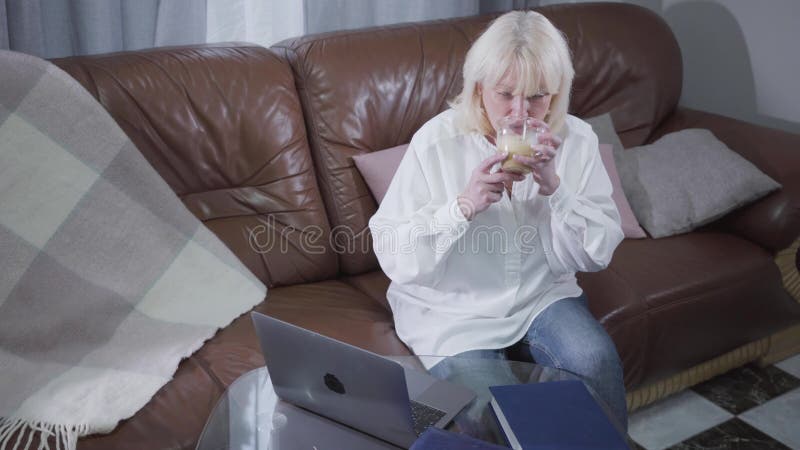 Vista superior de madura caucásica mujer vestida de forma casual tomando café y navegando por Internet Jubilado rubio de mayor ed almacen de metraje de vídeo