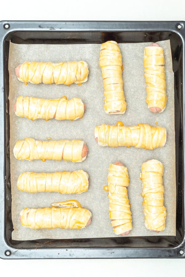 Top view of a baking sheet with sausages in raw dough greased with egg yolk. Cooking sausage in dough at home. Top view of a baking sheet with sausages in raw dough greased with egg yolk. Cooking sausage in dough at home.