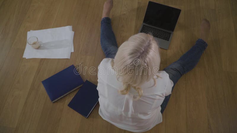 Vista superior de una mujer caucásica madura en jeans y camisa blanca sentada en el suelo de madera Mujer jubilada con aspecto po almacen de video