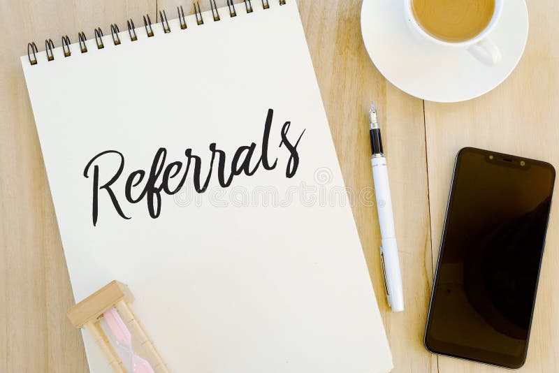 Top view of sand clock,pen,mobile phone,a cup of coffee and notebook written with Referrals. Top view of sand clock,pen,mobile phone,a cup of coffee and notebook written with Referrals