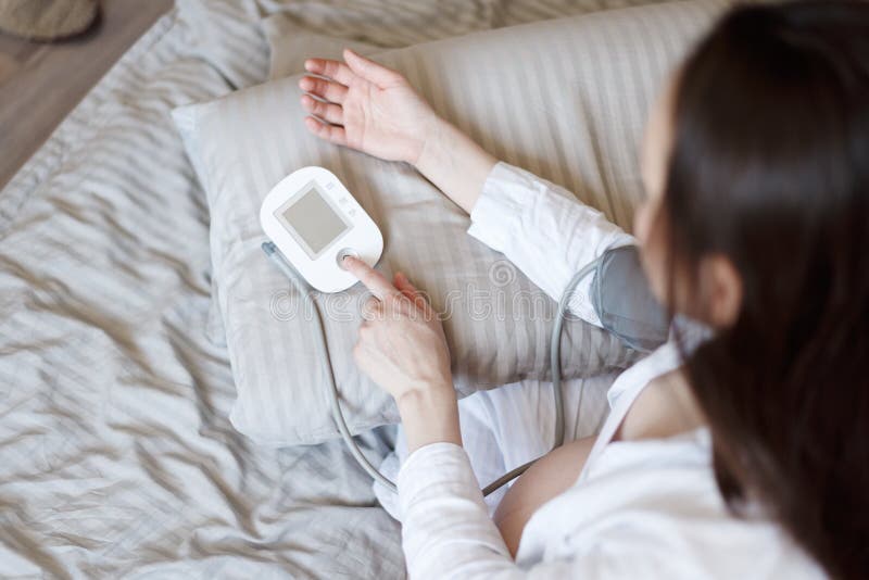 Vista superiore di pressione sanguigna di misurazione del letto castana della donna immagini stock libere da diritti Vista superiore di pressione sanguigna di misurazione del letto castana della donna immagini stock libere da diritti