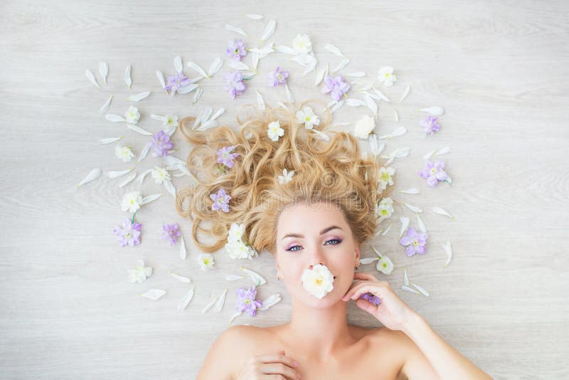 VISTA SUPERIORE: Il ritratto della ragazza bionda caucasica con il fiore in una bocca su un pavimento con un campo fiorisce immagine stock VISTA SUPERIORE: Il ritratto della ragazza bionda caucasica con il fiore in una bocca su un pavimento con un campo fiorisce immagine stock