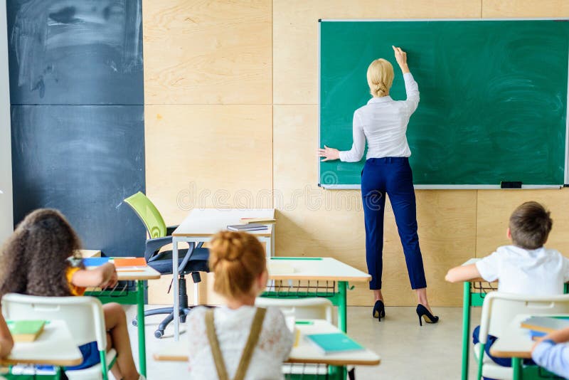 vista traseira dos alunos que olham o professor quando ela que escreve fotografia de stock vista traseira dos alunos que olham o professor quando ela que escreve fotografia de stock