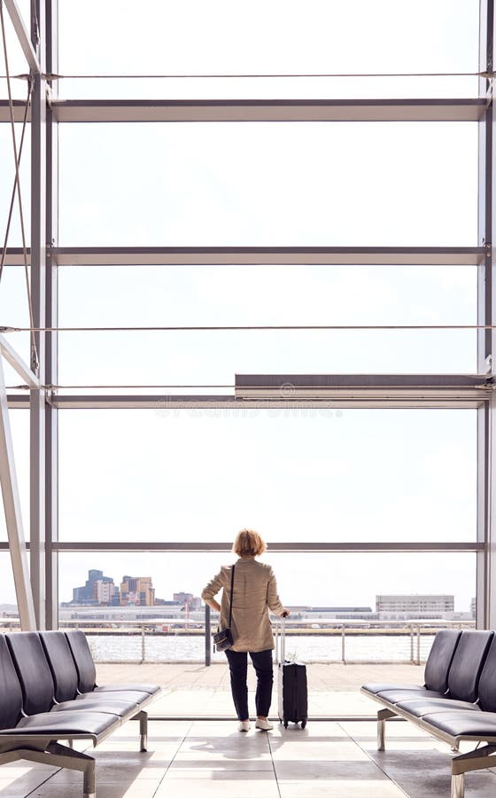 Vista Trasera De Una Mujer De Negocios Con Equipaje Parado Por Una Ventana En El Salón De Salida Del Aeropuerto imagen de archivo libre de regalías Vista Trasera De Una Mujer De Negocios Con Equipaje Parado Por Una Ventana En El Salón De Salida Del Aeropuerto imagen de archivo libre de regalías