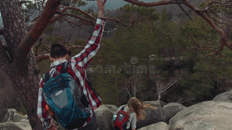 Vista trasera de una trayectoria complicada de la montaña, y gente joven que la sube abajo Un turista joven ase la rama de un vie