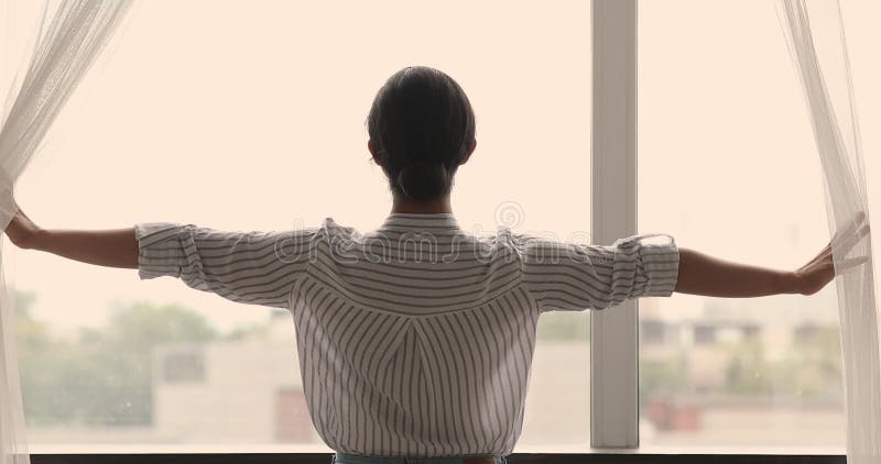 Vista trasera mujer joven abriendo cortinas acogedor nuevo día metrajes