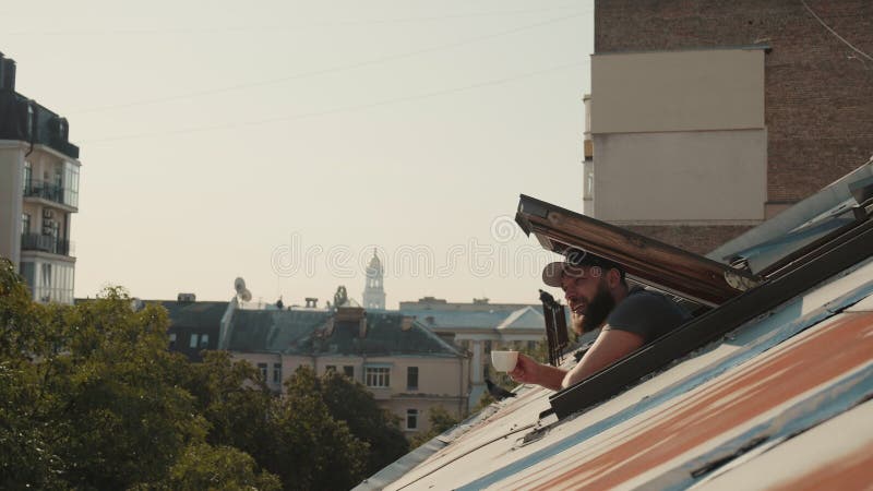 Vistas a los tejados. un joven apuesto abre una ventana que le saca la cabeza y disfruta de una taza de café con vistas a lviv