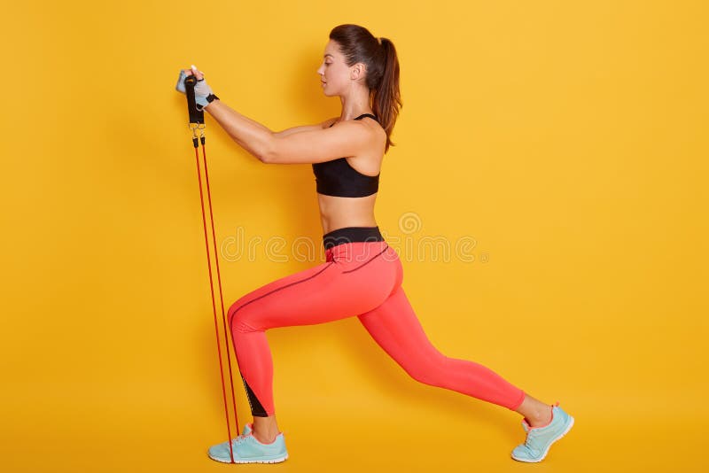 Visão completa da jovem morena vestida de roupa de exercício elegante e esticada na posição do almoço da perna com fotografia de stock Visão completa da jovem morena vestida de roupa de exercício elegante e esticada na posição do almoço da perna com fotografia de stock