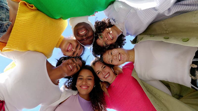 Visão de baixo ângulo de um grupo diversificado de jovens mulheres se abraçando ao ar livre