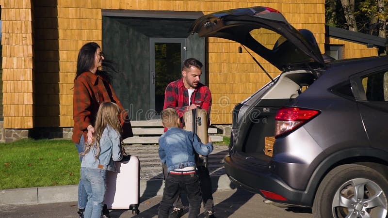 Visão frontal de uma família sorridente e bonita que carregava as malas no porta-malas antes da viagem conjunta de carro