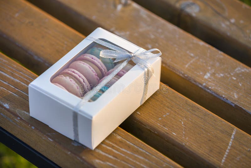 Vit gåvaask för papp med färgrika handgjorda macaronkakor på träbänk utomhus arkivfoto
