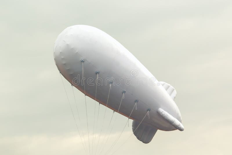 Vit uppblåsbar dirigible med ett ställe för en logo på en bakgrund av en grå himmel arkivbild Vit uppblåsbar dirigible med ett ställe för en logo på en bakgrund av en grå himmel arkivbild