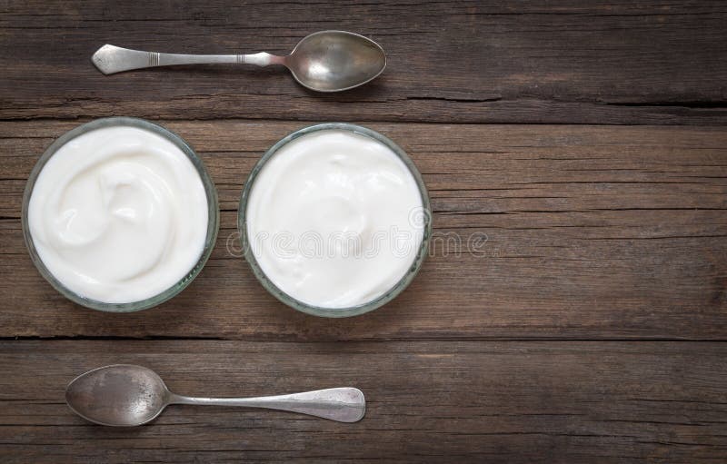 Vita exponeringsglasbunkar för yoghurt itu på det gamla träskrivbordet med två skedar bredvid royaltyfria foton Vita exponeringsglasbunkar för yoghurt itu på det gamla träskrivbordet med två skedar bredvid royaltyfria foton