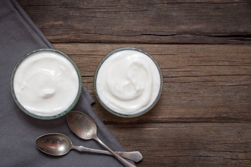 Vita exponeringsglasbunkar för yoghurt itu på det gamla träskrivbordet med två skedar bredvid royaltyfria foton Vita exponeringsglasbunkar för yoghurt itu på det gamla träskrivbordet med två skedar bredvid royaltyfria foton