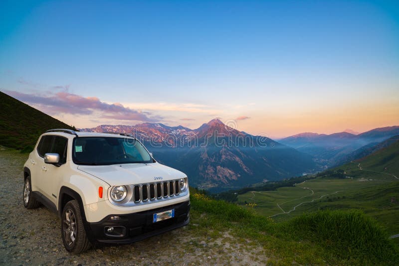 Vita Jeep Renegade som parkeras på grusvägen på panoramautsiktpunkt på de italienska fjällängarna från över Färgrik himmel på sol royaltyfri bild Vita Jeep Renegade som parkeras på grusvägen på panoramautsiktpunkt på de italienska fjällängarna från över Färgrik himmel på sol royaltyfri bild