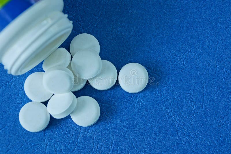 Vita runda piller och en plast- flasklögn på en blå tabell fotografering för bildbyråer Vita runda piller och en plast- flasklögn på en blå tabell fotografering för bildbyråer