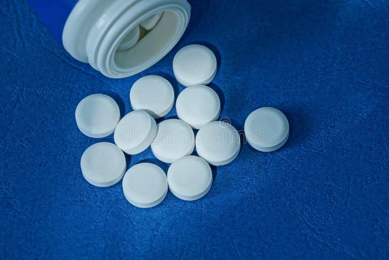 Vita runda piller och en plast- flasklögn på en blå tabell arkivfoton Vita runda piller och en plast- flasklögn på en blå tabell arkivfoton