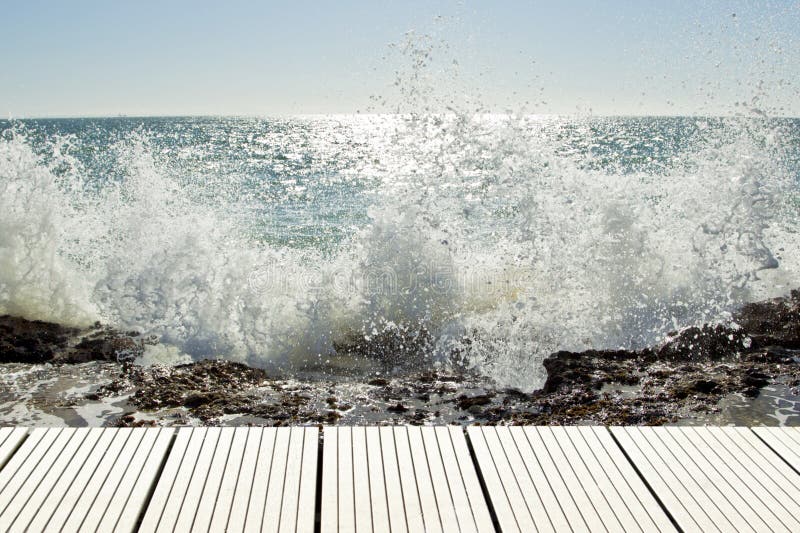 Vitt däck som förbiser havet. Vitt trädäck som förbiser ett härligt hav för hög kontrast med vågor som bryter på middagar