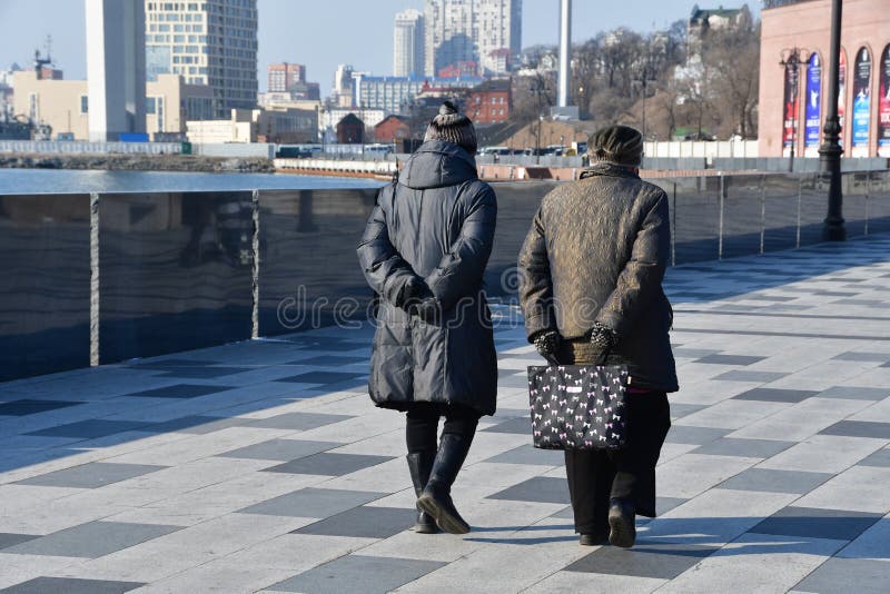 Vladivostok Ryssland, Januari 19, 2019 Två äldre kvinnor som promenerar invallningen av kronprinsen Tsesarevich i solig seger arkivbild Vladivostok Ryssland, Januari 19, 2019 Två äldre kvinnor som promenerar invallningen av kronprinsen Tsesarevich i solig seger arkivbild