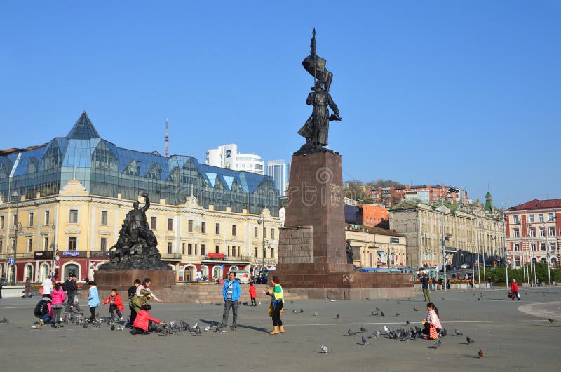 Vladivostok, Rússia, outubro, 25, 2017 Turistas chineses que alimentam pombos no quadrado central de Vladivostok perto do monumen foto de stock Vladivostok, Rússia, outubro, 25, 2017 Turistas chineses que alimentam pombos no quadrado central de Vladivostok perto do monumen foto de stock