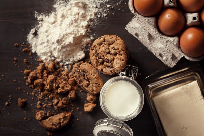 Vlak leg van Eigengemaakte chocoladeschilferkoekjes met fles van melk, witte bloem, verse eieren, boter en crumbs op plattelander royalty-vrije stock fotografie Vlak leg van Eigengemaakte chocoladeschilferkoekjes met fles van melk, witte bloem, verse eieren, boter en crumbs op plattelander royalty-vrije stock fotografie