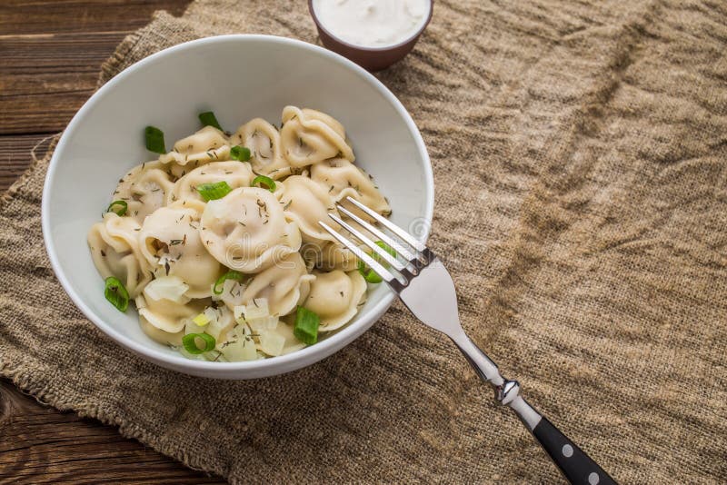 Meat dumplings - russian pelmeni, ravioli with meat on a white plate on a wooden background. Meat dumplings - russian pelmeni, ravioli with meat on a white plate on a wooden background