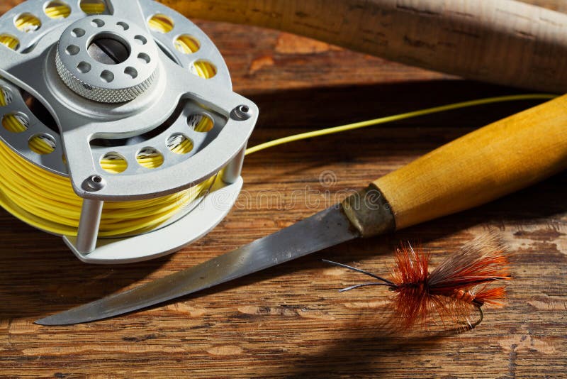 Horizontal shot of a fly fishing reel, fly, rod handle and yellow line on a wood table top. Horizontal shot of a fly fishing reel, fly, rod handle and yellow line on a wood table top