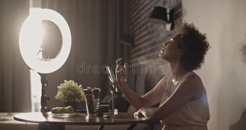 Vlogger de beauté noire application spray faciale près d'une lampe à anneau banque de vidéos