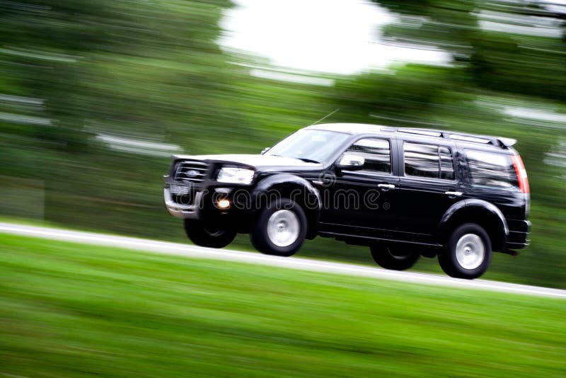 A black SUV rushing away on a countryside road. A black SUV rushing away on a countryside road