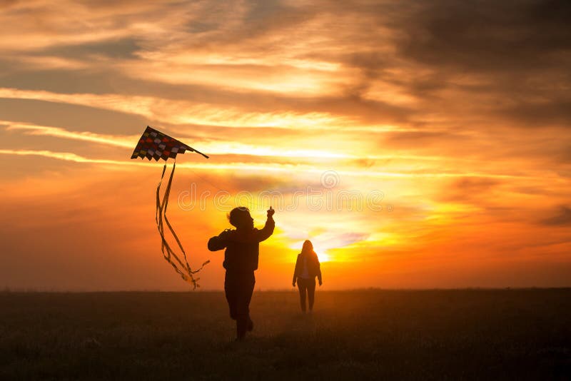 Voando um papagaio A menina e o menino voam um papagaio no campo infinito Por do sol brilhante Silhuetas dos povos contra o c?u fotos de stock Voando um papagaio A menina e o menino voam um papagaio no campo infinito Por do sol brilhante Silhuetas dos povos contra o c?u fotos de stock