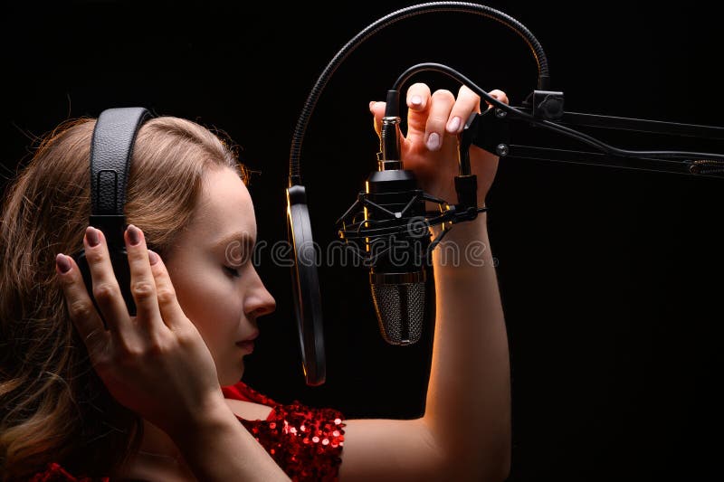 The vocalist sings in the studio in a studio microphone. In headphones, on a black background. Artist, recording an album, disc.