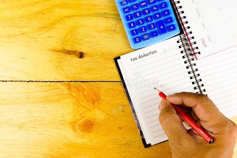 Conceptual image of tax return to tax authority in April. Fingers holding pen writing on blank note book. Calculator visible. Selective focus on beads. Wooden background. Conceptual image of tax return to tax authority in April. Fingers holding pen writing on blank note book. Calculator visible. Selective focus on beads. Wooden background