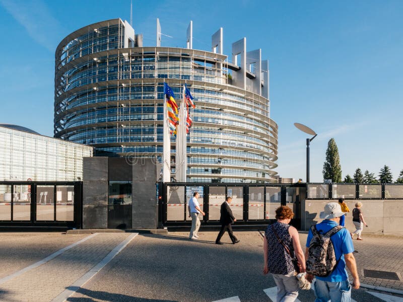 STRASBOURG, FRANCE - MAY 26, 2017: People walking in front of European Parliament building white EU flag at half mast in memory of victims terrorist explosion Manchester Arena Ariana Grande concert. STRASBOURG, FRANCE - MAY 26, 2017: People walking in front of European Parliament building white EU flag at half mast in memory of victims terrorist explosion Manchester Arena Ariana Grande concert