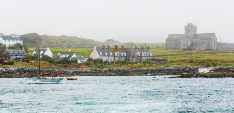 Panorama of Iona island natural port close to Mull, in the Inner Hebrides of Scotland, with a moored vintage schooner sailboat. Foggy, evocative atmosphere wraps the touristic medieval Iona Abbey. Panorama of Iona island natural port close to Mull, in the Inner Hebrides of Scotland, with a moored vintage schooner sailboat. Foggy, evocative atmosphere wraps the touristic medieval Iona Abbey.