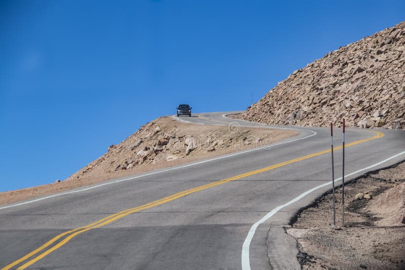 Voiture arrondissant le coude fermé avec la descente raide sur la route dangereuse de montagne avec le ciel bleu derrière photos stock Voiture arrondissant le coude fermé avec la descente raide sur la route dangereuse de montagne avec le ciel bleu derrière photos stock