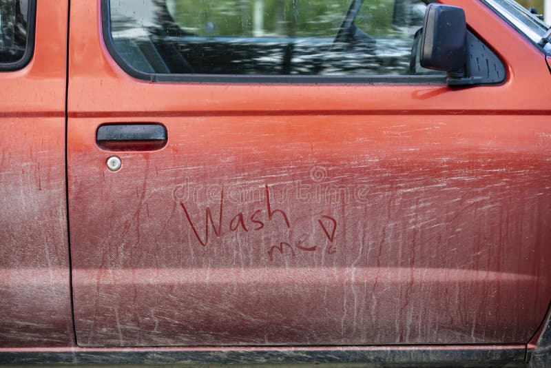 Very dirty red car. The door has text; Wash me!. Very dirty red car. The door has text; Wash me!