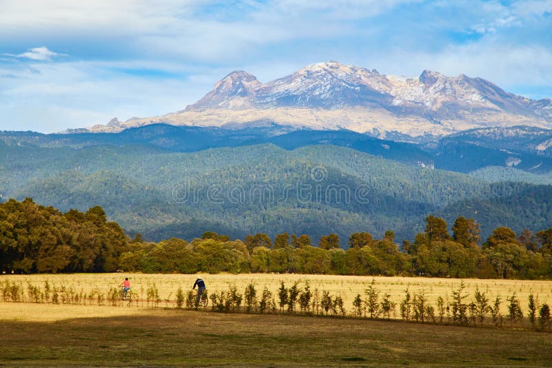 Photograph of the mexican volcano Iztaccihuatl the sleepy woman (la mujer dormida) in Puebla Mexico seen from Amecameca and two persons biking.