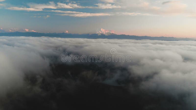 Voler au-dessus des nuages au crépuscule ou à l'aube Voler au-dessus des nuages en direction d'une haute montagne neigeuse aérien banque de vidéos