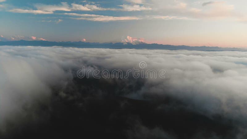 Voler au-dessus des nuages au crépuscule ou à l'aube Voler au-dessus des nuages en direction d'une haute montagne neigeuse aérien clips vidéos