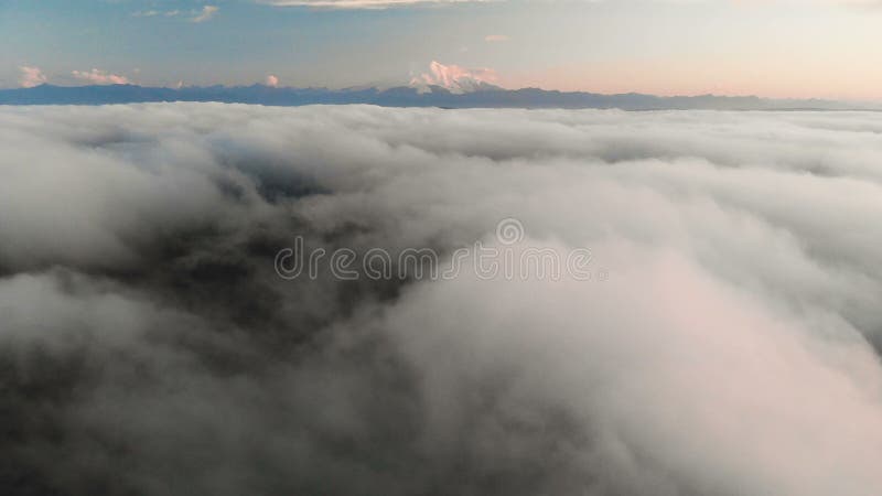 Voler au-dessus des nuages au crépuscule ou à l'aube Voler au-dessus des nuages en direction d'une haute montagne neigeuse aérien banque de vidéos