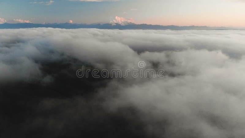 Voler au-dessus des nuages au crépuscule ou à l'aube Voler au-dessus des nuages en direction d'une haute montagne neigeuse aérien banque de vidéos