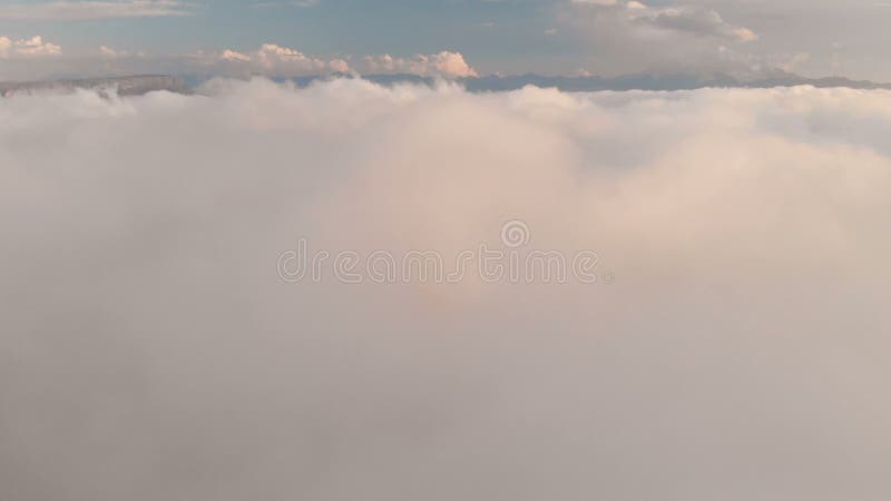 Voler au-dessus des nuages au crépuscule ou à l'aube Voler au-dessus des nuages en direction d'une haute montagne neigeuse aérien banque de vidéos