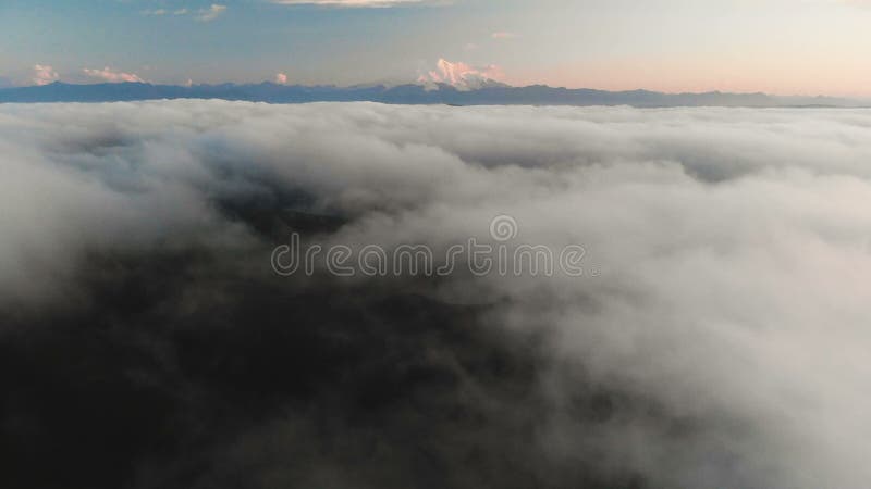 Voler au-dessus des nuages au crépuscule ou à l'aube Voler au-dessus des nuages en direction d'une haute montagne neigeuse aérien banque de vidéos