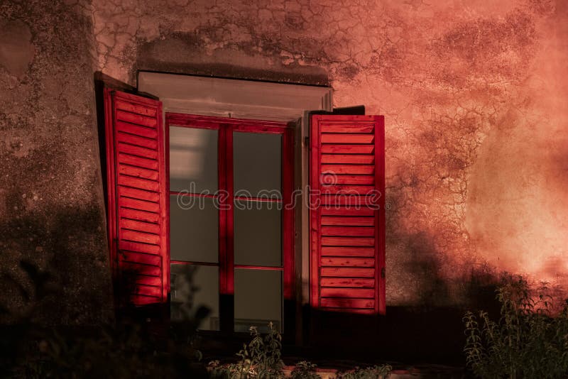 Volets rouges la nuit sur la ferme toscane. Une paire de volets rouges vifs attachés à une fenêtre sur une ancienne ferme en toscane, italie, sont éclairés par la lumière artificielle