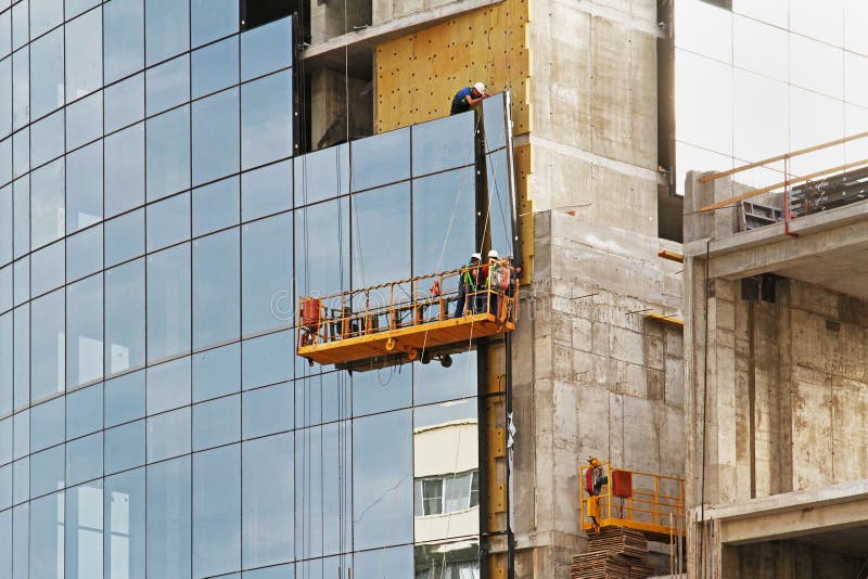 Workers on the scaffold elevator install glass window on facade of new building in Volgograd