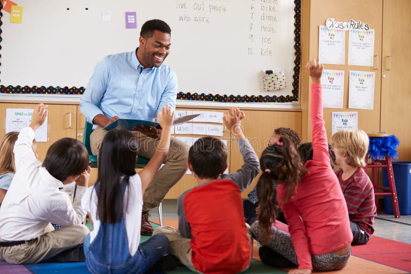 Volksschule scherzt das Sitzen um Lehrer in einem Klassenzimmer lizenzfreies stockbild Volksschule scherzt das Sitzen um Lehrer in einem Klassenzimmer lizenzfreies stockbild